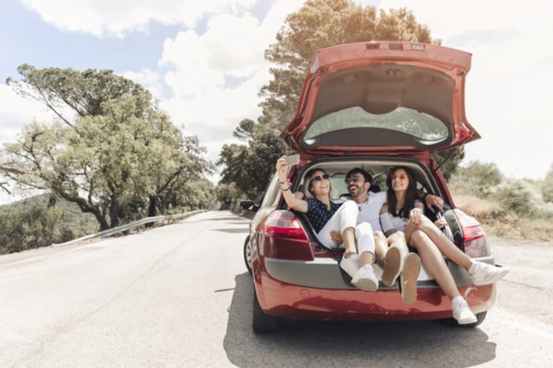 three-friends-sitting-together-car-trunk-taking-self-portrait